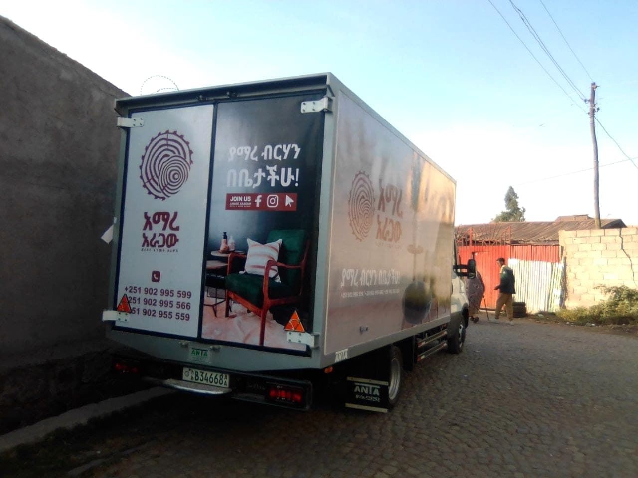 Rear doors of a box truck printed with the Amare Aragaw mark, an interior photograph and social handles