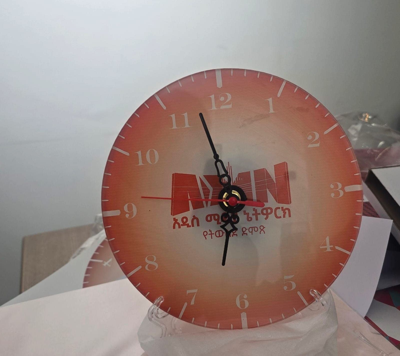 Round glass desk clock printed with the Addis Media Network logo on a warm orange gradient face