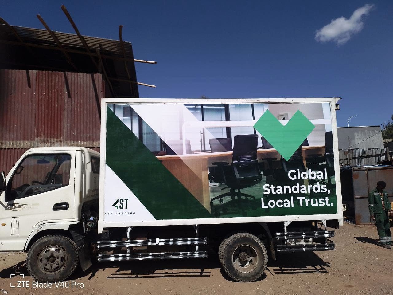Full side view of the AST Trading box truck against a blue sky, showing the complete printed panel