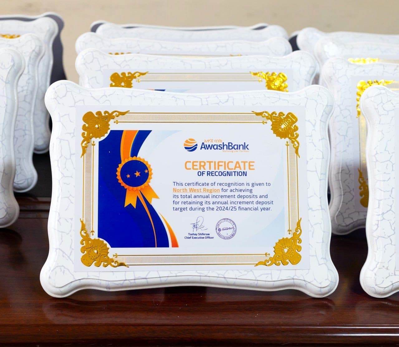 Row of white crackle-finish presentation plaques holding Awash Bank certificates of recognition with gold corner ornaments