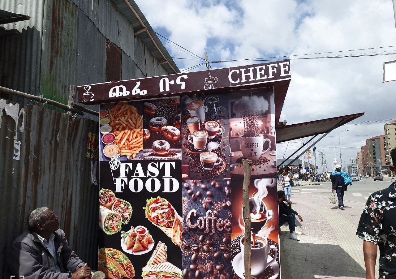 Roadside coffee and fast-food kiosk wrapped in printed panels of coffee and food photography under a Chefe Buna fascia