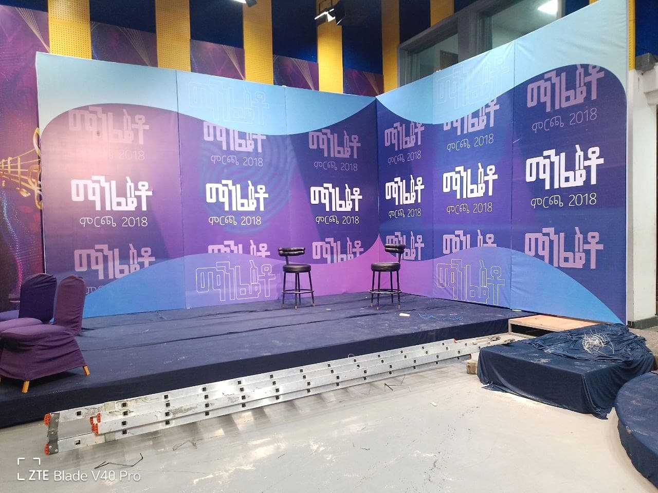 Curved purple and blue studio backdrop for Fana’s Manchet 2018 programme, with two stools on a low stage