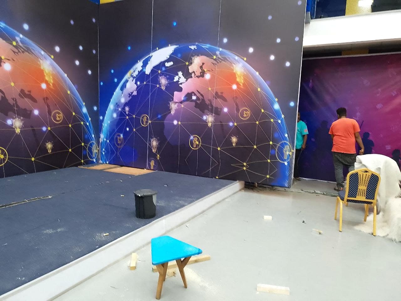 Large printed globe backdrop panels being assembled on a stage, with the crew fitting the adjoining purple panel