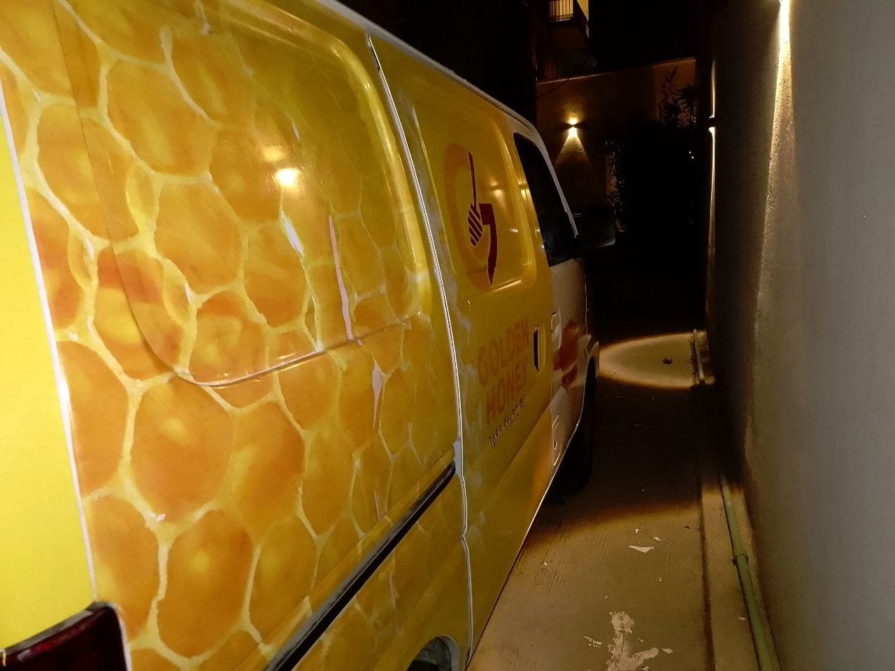 Side of a delivery van fully wrapped in a golden honeycomb graphic with the Golden Honey logo on the rear door