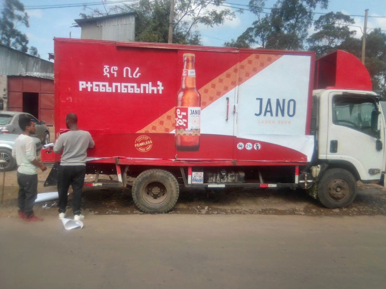 Two of the team applying a red Jano Lager Beer wrap to the side of a distribution truck at the roadside