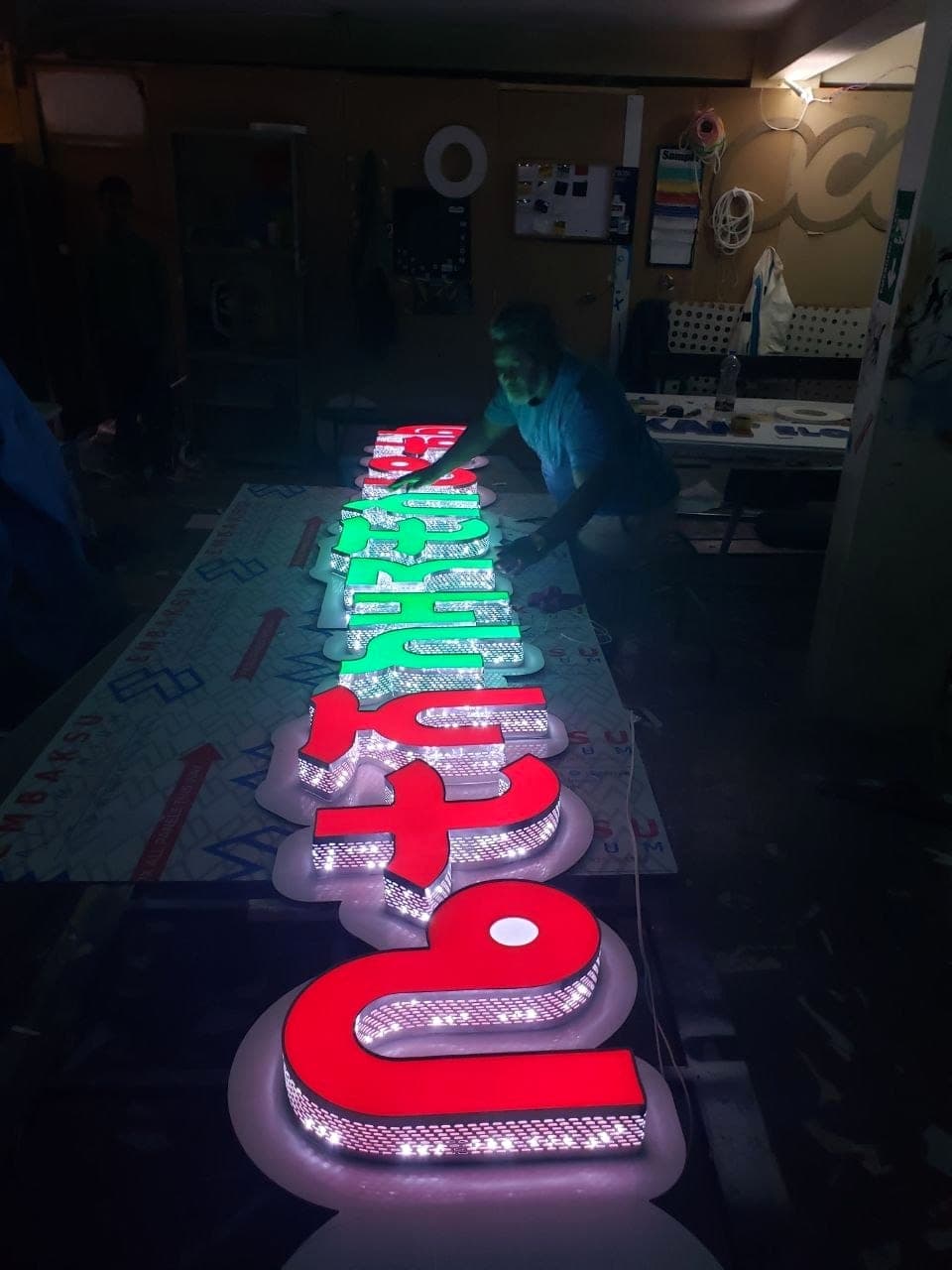 A row of large red and green Amharic channel letters lit for the first time on the workshop bench, LED strips visible inside the returns
