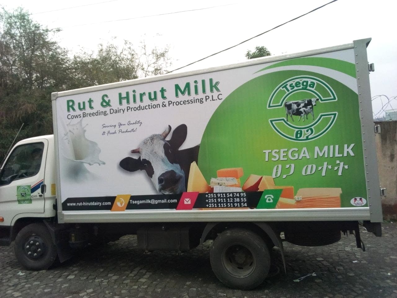 White and green box truck printed for Rut & Hirut Milk, with the Tsega Milk mark, a dairy cow and cheese photography across the panel