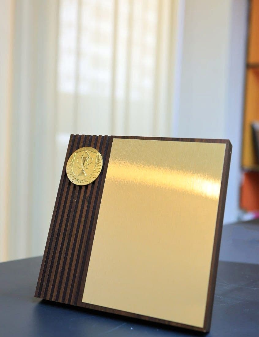 Ribbed dark wood plaque with a brushed brass engraving plate and a small gold trophy medallion